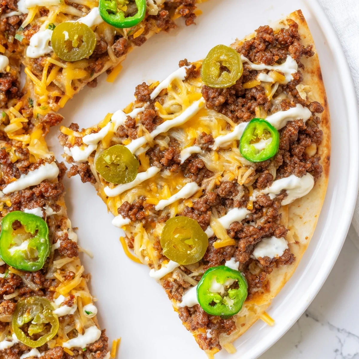 Mouthwatering Ground Beef Taco Pizza ready to slice, with a creamy sour cream drizzle on top.