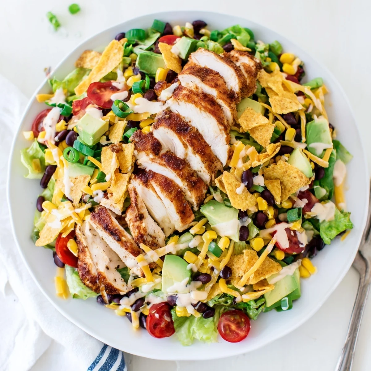Vibrant Crunchy Taco Chicken Salad in a white bowl, featuring sliced seasoned chicken, black beans, corn, and diced avocado with shredded cheese.
