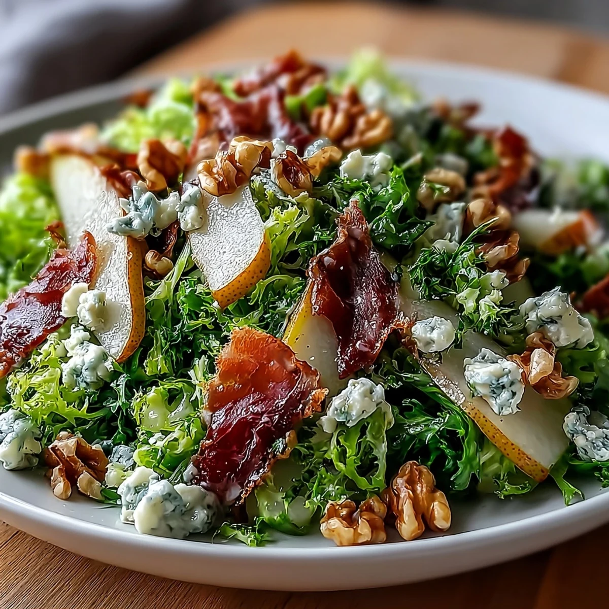 An elegant serving of Frisée, Pear, Blue Cheese, and Crispy Prosciutto Salad arranged on a white platter, topped with toasted walnuts and drizzled with a tangy honey-mustard vinaigrette.