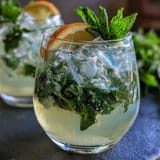A tall glass of iced lavender lemonade with fresh mint, garnished with lemon slices and mint sprigs, perfect for spring refreshment.