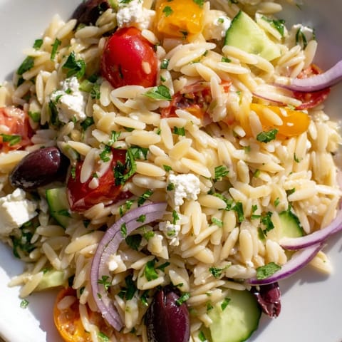 Greek Orzo Salad in a white bowl, garnished with parsley and lemon, perfect for summer picnics.  