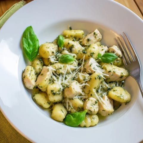 A close-up of creamy pesto gnocchi with chicken, garnished with fresh basil and a sprinkle of Parmesan, perfect for weeknight comfort.