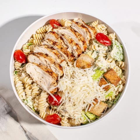 A vibrant Caesar Pasta Chicken Bowl garnished with freshly grated Parmesan and crunchy garlic croutons, perfect for a weeknight meal.
