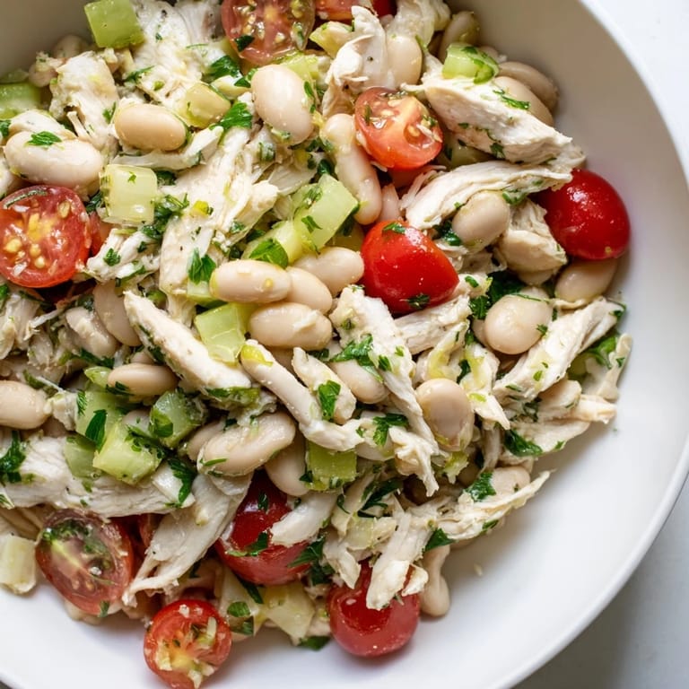 A close-up of Lemony White Bean Chicken Salad highlights chopped parsley, diced red onion, and juicy cherry tomatoes, ready for a light lunch or meal prep.