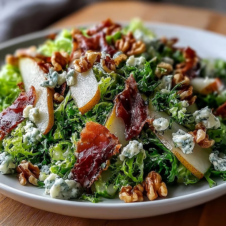 An elegant serving of Frisée, Pear, Blue Cheese, and Crispy Prosciutto Salad arranged on a white platter, topped with toasted walnuts and drizzled with a tangy honey-mustard vinaigrette.