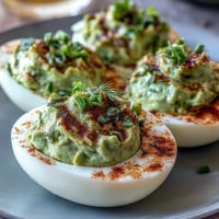 Creamy green avocado deviled eggs garnished with fresh herbs, perfect for spring parties and healthy snacking.